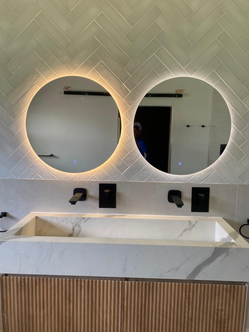 Dual round LED backlit bathroom mirrors with warm glow, marble vanity and herringbone tiles