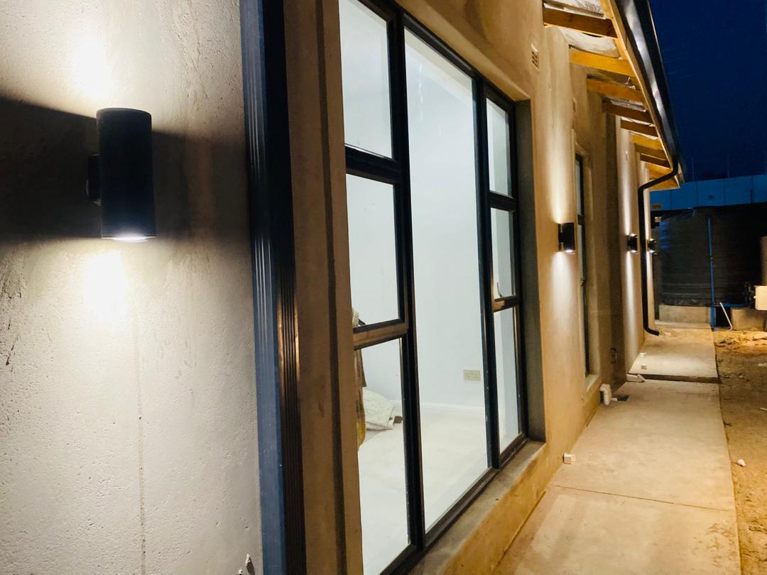Exterior up-down wall sconces glowing on rendered wall of new residential build at night