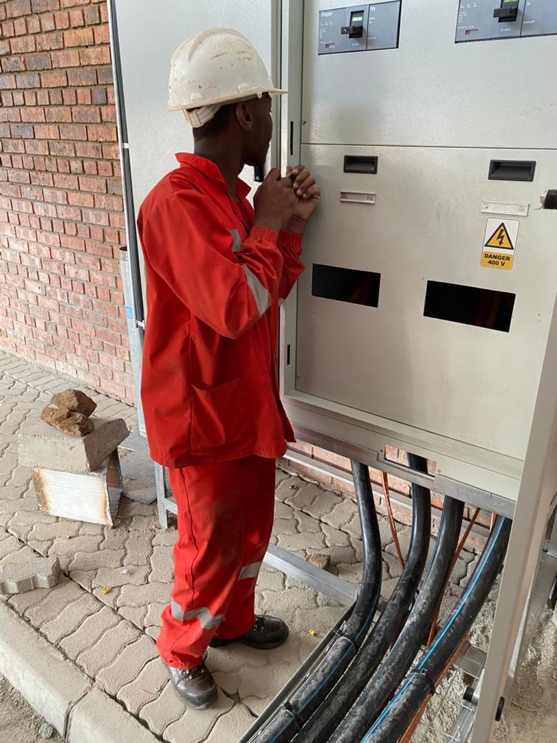 Dosmac trade-tested artisan in red overalls and hard hat working on 400V Hager industrial switchgear