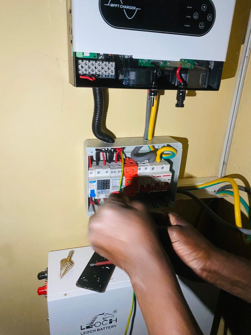 Hands wiring DC combiner box with MPPT solar charger above and Leoch battery below