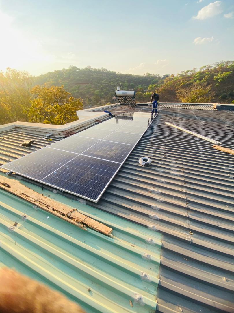 Solar panels being commissioned on corrugated iron roof at golden hour, Zimbabwe hills behind